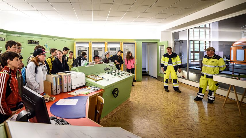 Visita alla centrale di comando di una centrale elettrica con giovani e operatori in abbigliamento protettivo.