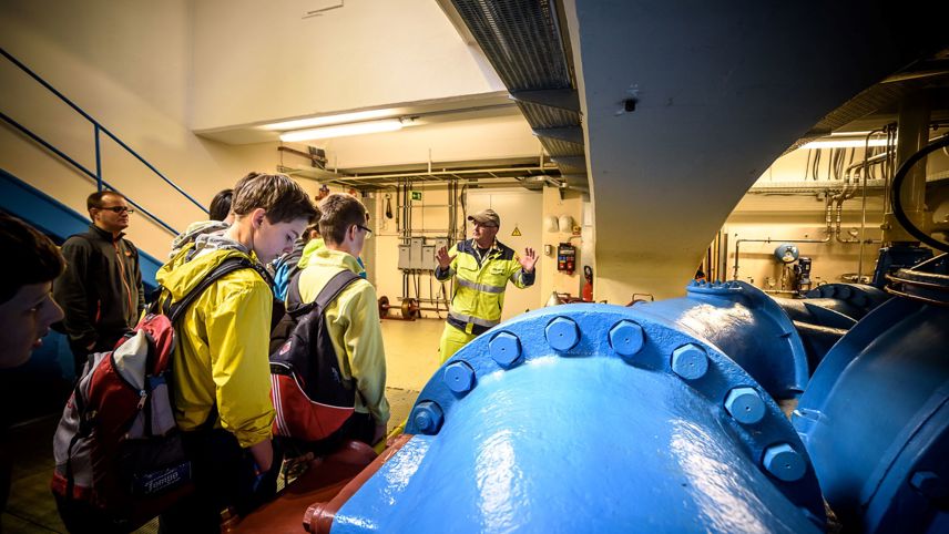 Visita guidata in una centrale idroelettrica con giovani davanti a una grande condotta della turbina.