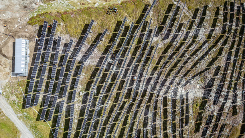 Luftaufnahme von Madrisa Solar: Solarmodulreihen auf alpinem Hang mit Technikgebäude.
