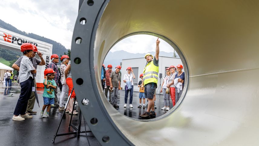 Tag der offenen Tür im Kraftwerk Robbia: Besuchergruppe mit Helmen, Mitarbeitender erklärt Anlage durch ein Rohr.