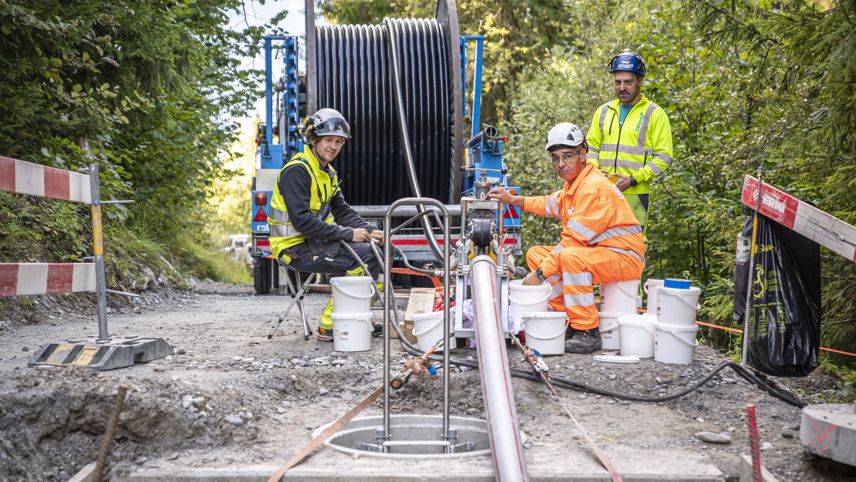 Bautrupp arbeitet an einer Leitungsverkabelung; Kabeltrommel und Geräte stehen an einer Waldstrasse.