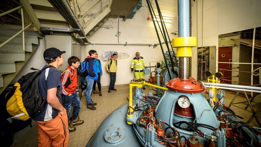 Giovani durante una visita guidata in una centrale elettrica, osservano un impianto tecnico con un esperto.
